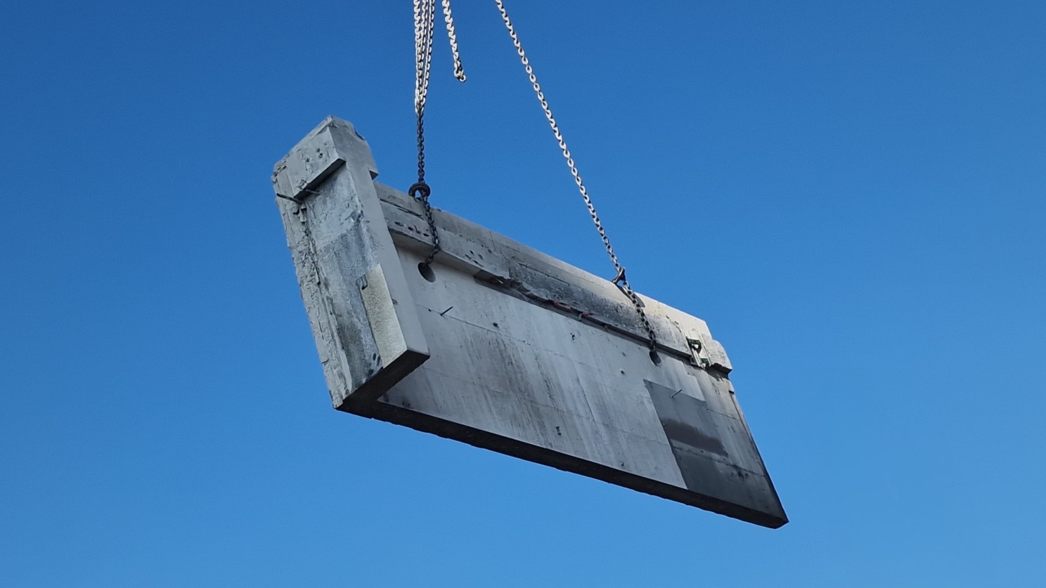 A recovered concrete wall panel suspended against a blue sky